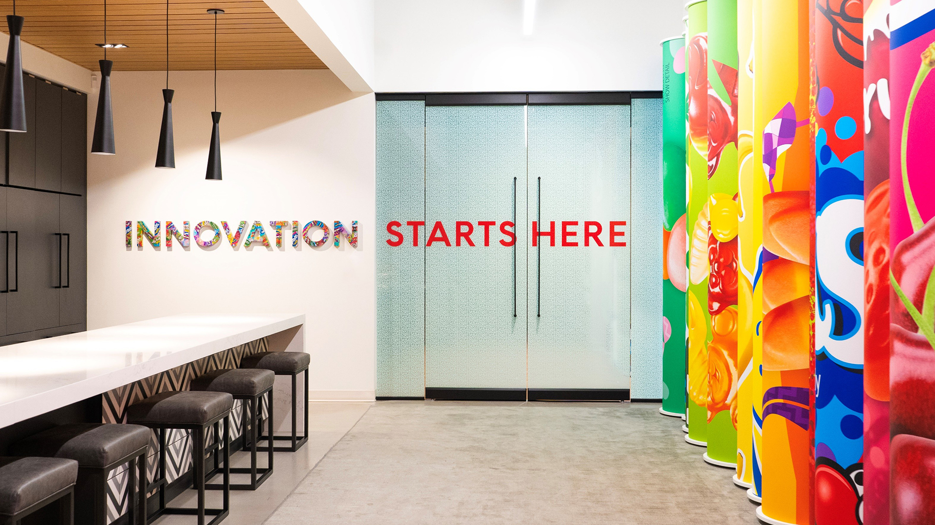 Breakroom galley with table and chairs on left and wall treatment of colorful candy logos on the right overlayed with the words Innovation starts here