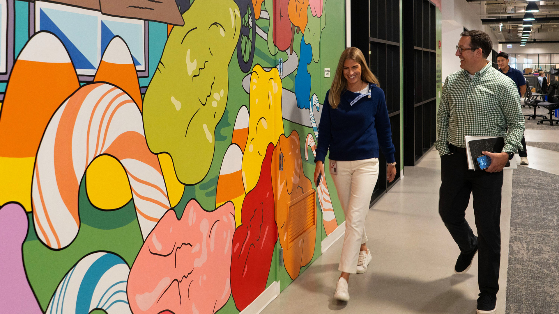 Male and female walking beside a colorful mural in an office environment