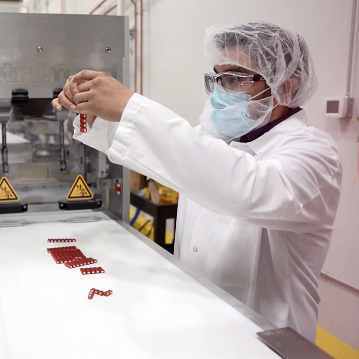 Ferrara employee wearing a hairnet, face mask and white coat in a quality lab testing red candies