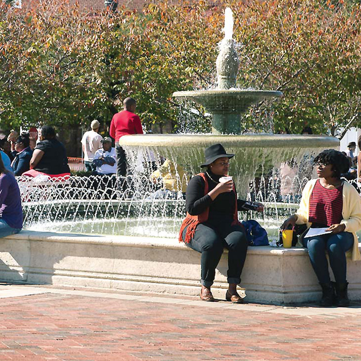 people gathered around and sitting on the edge of a large park fountain